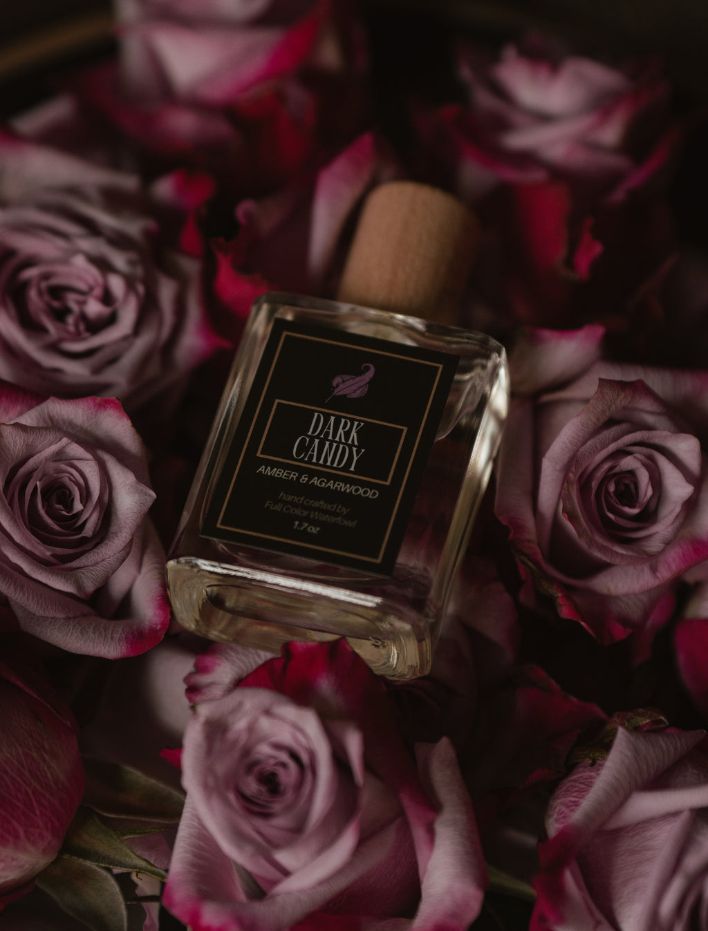 Perfume bottle labeled 'Dark Candy' surrounded by pink roses