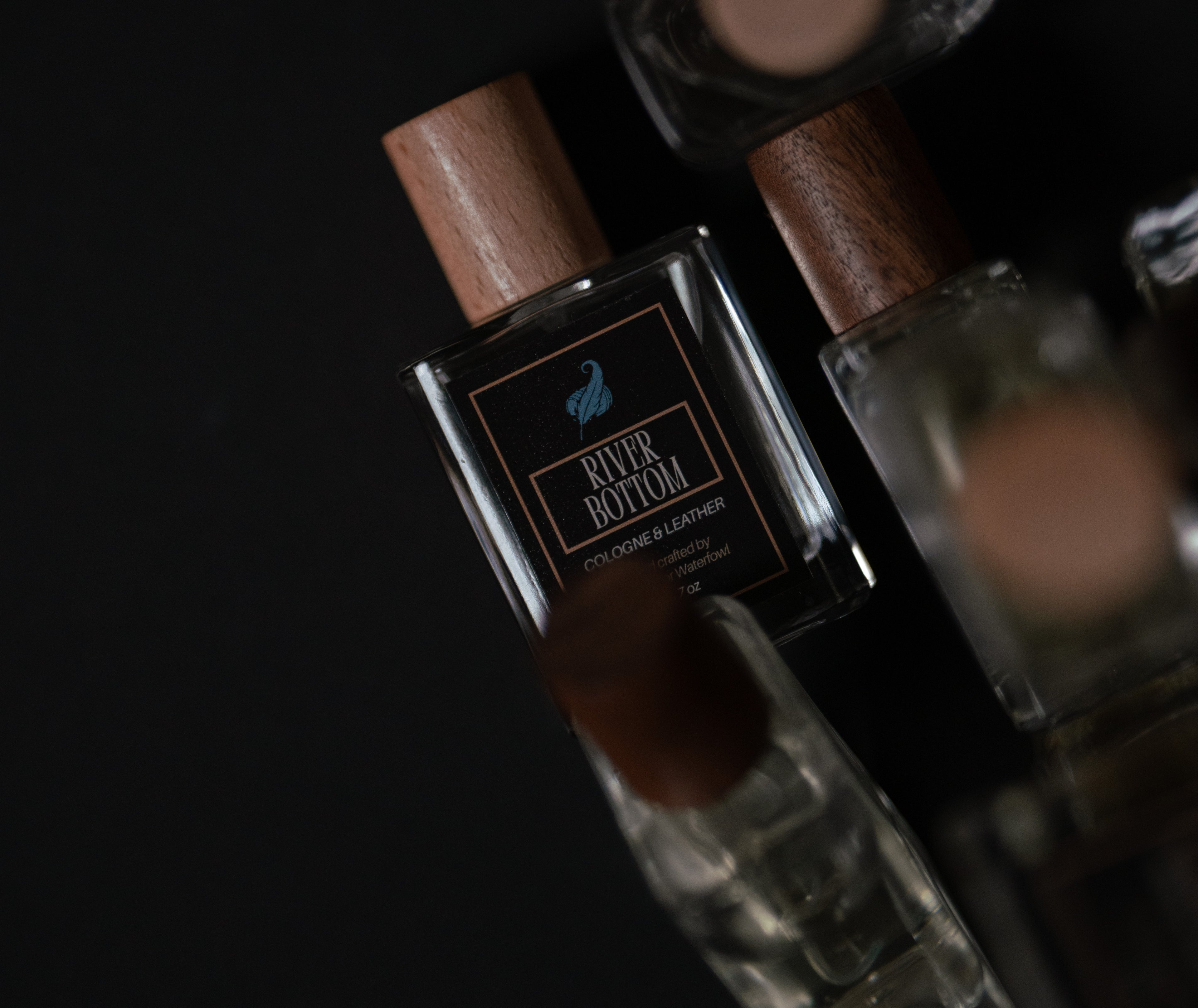 Perfume bottle with wooden cap and visible brand name River Bottom by Full Color Waterfowl on a dark background surrounded by other perfumes 